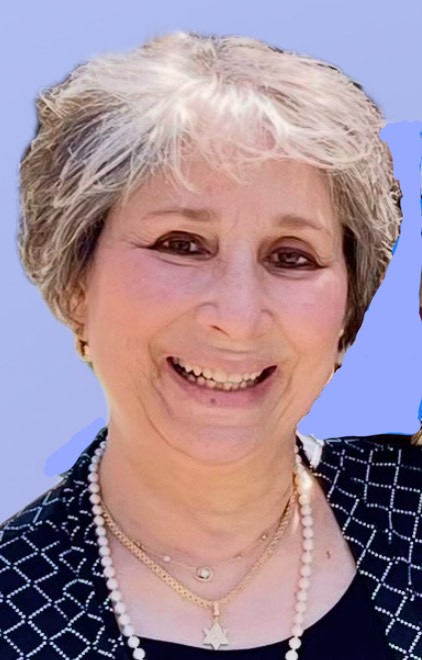 Smiling white woman with short gray hair wearing a pearl necklace, a patterned shirt and a Star of David necklace.