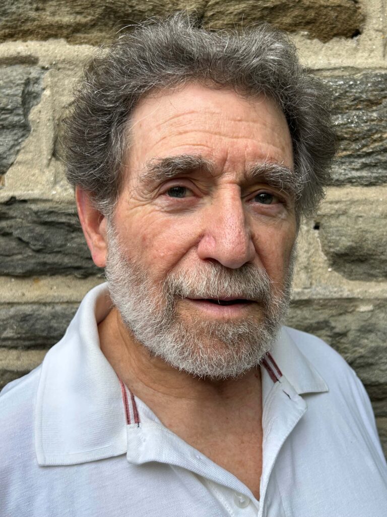 White man with black hair and a gray beard wearing a white collared shirt