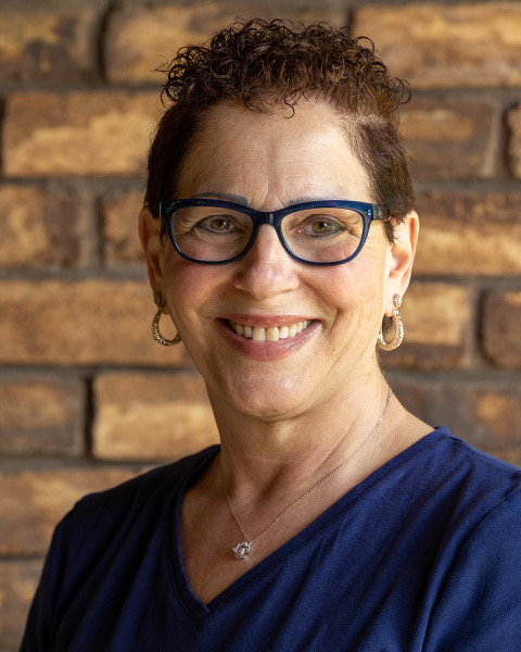 Professional headshot of Nancy Ginsberg with a brown brick background.